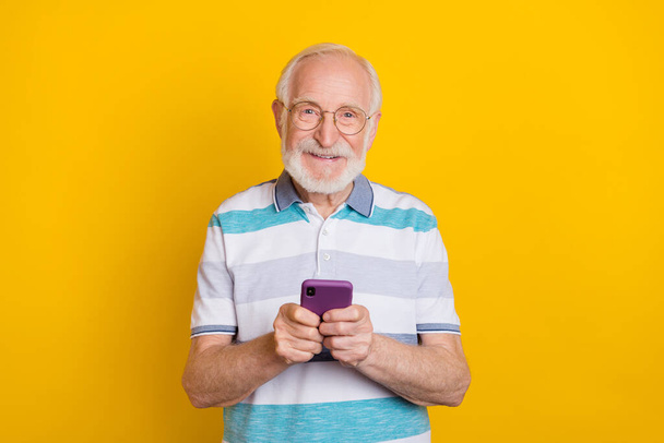 Portrait of attractive cheerful grey haired man using device post 5g smm isolated over bright yellow color background - Valokuva, kuva