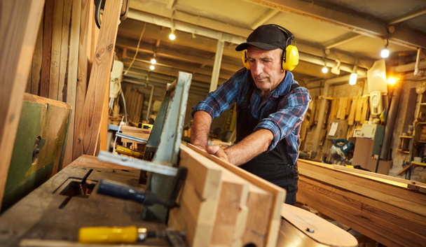 Hoge timmerman in uniform werkt op een houtbewerkingsmachine bij de houtbewerkingsindustrie - Foto, afbeelding