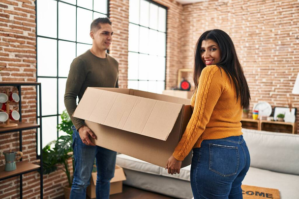 Homem e mulher casal sorrindo confiante segurando pacote em nova casa - Foto, Imagem