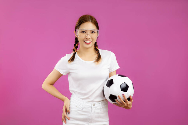 Asian Young woman in white t-shirt over isolated pink background holding a soccer ball and looking at camera, football concept - Photo, image