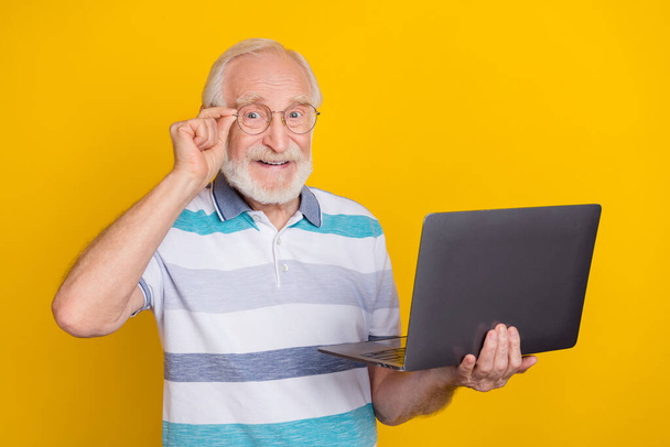 Portrait of attractive cheerful grey haired man using laptop touching specs isolated over bright yellow color background - Fotó, kép