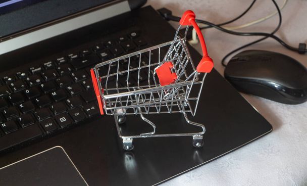 Pequeño carrito de compras en una computadora para simbolizar el comercio electrónico - Foto, Imagen
