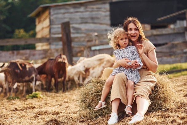 Young mother with her daughter is on the farm at summertime with goats. - Photo, image