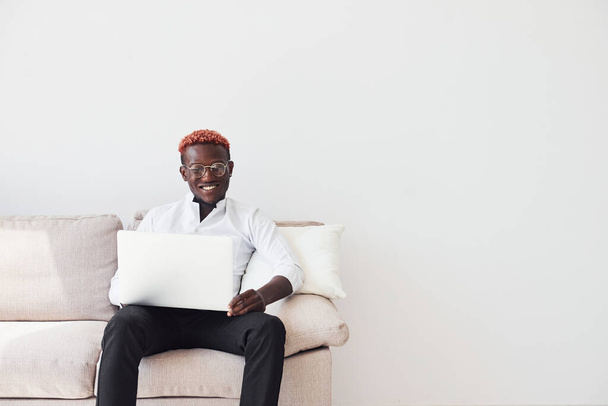 Young african american man in formal clothes sitting indoors with laptop in hands. - Fotoğraf, Görsel