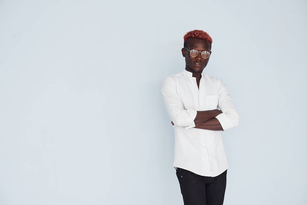 Young african american man in white formal clothes standing against wall indoors. - Фото, изображение