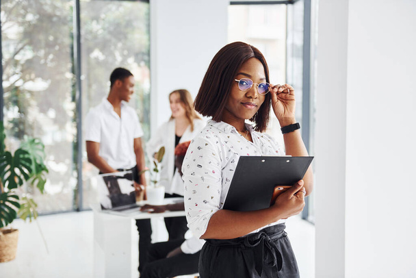 Beautiful woman in glasses in front of her colleagues. Group of african american business people working in office together. - Foto, afbeelding