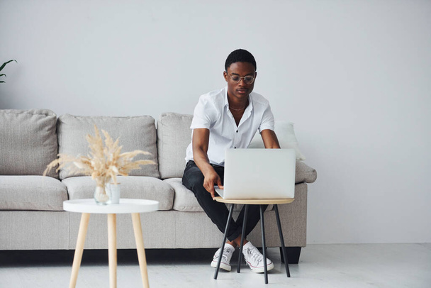 Молодой африканский американец в формальной одежде в помещении с ноутбуком в руках. - Фото, изображение