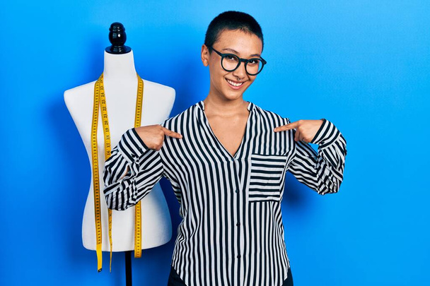 Beautiful hispanic woman with short hair standing by manikin looking confident with smile on face, pointing oneself with fingers proud and happy.  - Photo, Image