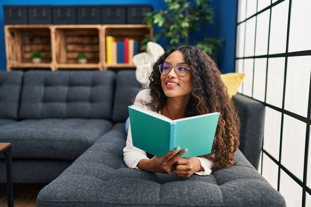 Jovem mulher latina lendo livro deitado no sofá em casa - Foto, Imagem