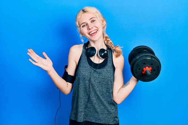 Beautiful caucasian sports woman with blond hair wearing sportswear using dumbbells celebrating achievement with happy smile and winner expression with raised hand  - Photo, image