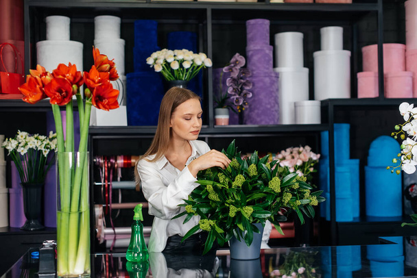 A young female florist takes care of flowers in a cozy flower shop and collects bouquets. Floristry and making of bukets in a flower shop. Small business. - Φωτογραφία, εικόνα
