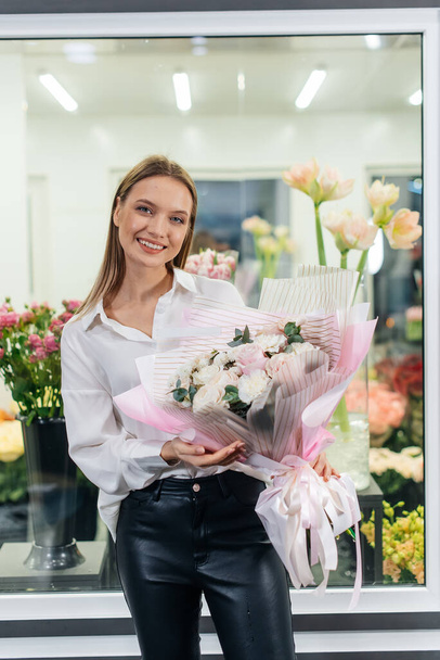 A young girl poses with a beautiful festive bouquet against the background of a cozy flower shop. Floristry and bouquet making in a flower shop. Small business. - Zdjęcie, obraz