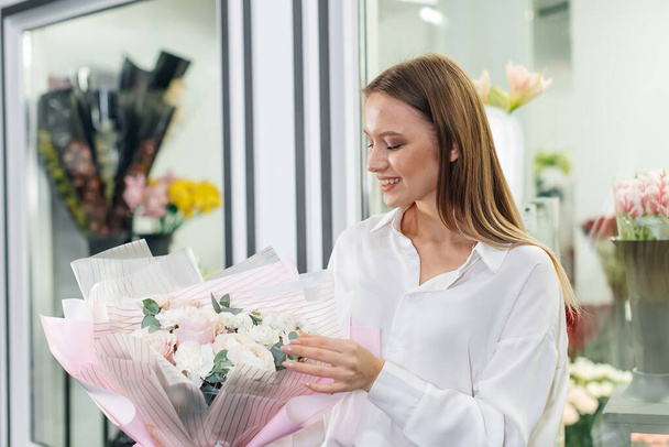 A young girl poses with a beautiful festive bouquet against the background of a cozy flower shop. Floristry and bouquet making in a flower shop. Small business. - Fotografie, Obrázek