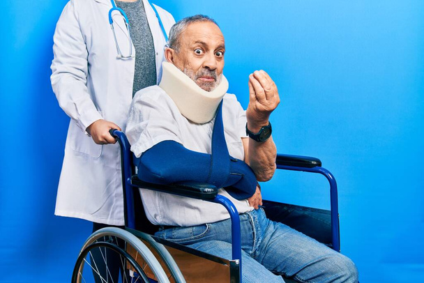 Pohledný starší muž s vousy sedí na invalidním vozíku s límcem na krku dělá peníze gesta rukama, žádá o výplatu mzdy, milionář podnikání  - Fotografie, Obrázek