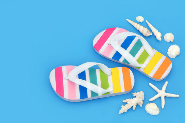 Rainbow striped flip flops on blue background with seashells. Trendy summer footwear for beach holiday vacation and LGBT themed concept. Copy space, top view. - Photo, Image