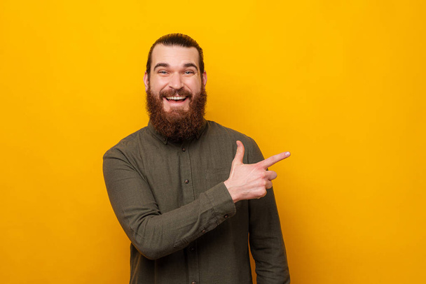 Ecstatic bearded man is pointing aside while smiling at the camera. - Photo, Image