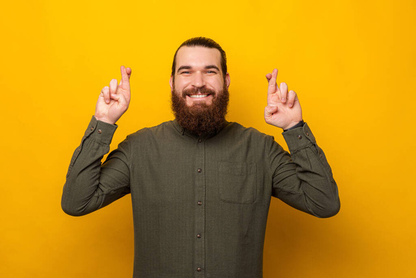 Young bearded man with exhilarated face is crossing fingers for a wish. - Photo, Image