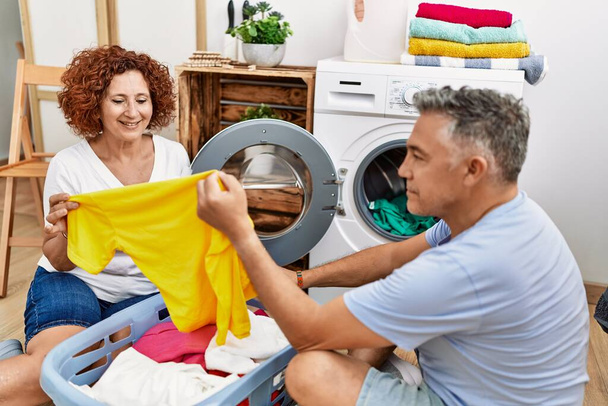 Középkorú férfi és nő pár kezében póló mosás ruhák a mosodában - Fotó, kép