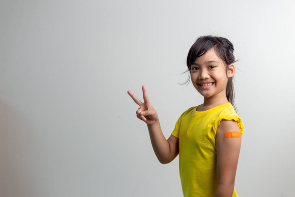 COVID 19 Vaccines for Kids концепт. Прочитайте портрет чарівної азіатської дівчини після отримання першої дози вакцини. Імуне, безпечне, доступне, знову до школи. - Фото, зображення