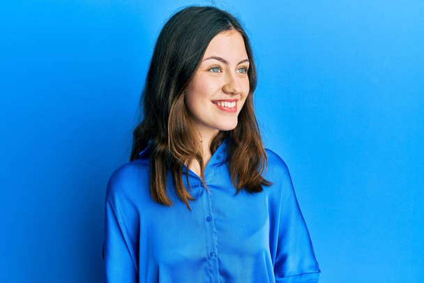 Fiatal barna nő visel alkalmi kék ing néz oldalra mosollyal az arcán, természetes kifejezés. nevetés magabiztos.  - Fotó, kép