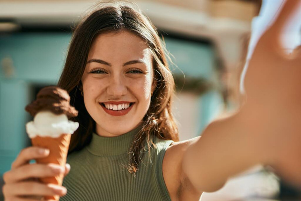 Jeune fille caucasienne manger de la crème glacée faire selfie par la caméra à la ville. - Photo, image