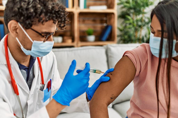Młody lekarz wstrzykuje covid-19 szczepionkę przeciw koronawirusowi kobiecie siedzącej na kanapie w klinice. - Zdjęcie, obraz