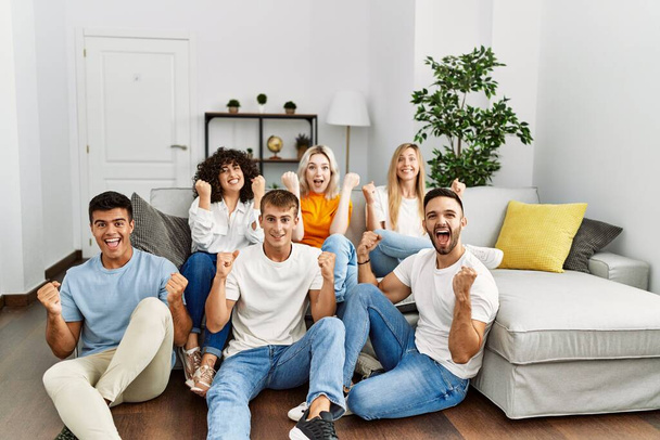 Ryhmä ihmisiä istuu sohvalla ja lattialla kotona huutaen ylpeä, juhlii voittoa ja menestystä hyvin innoissaan nostetaan kädet  - Valokuva, kuva