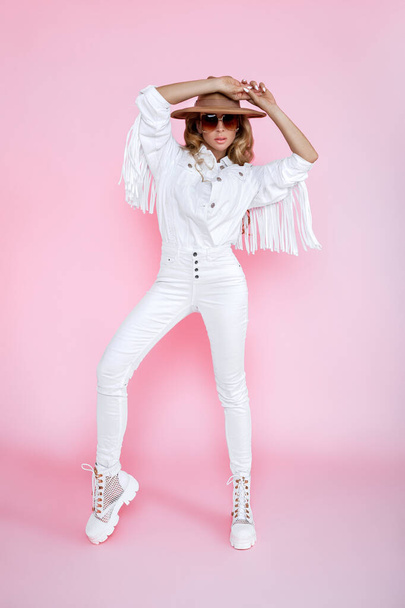 Spring fashion. Beautiful stylish female model in white trendy outfit in studio. Elegant woman in white fringe jacket and white boots on pink background. Studio shoot. Fashionable woman. - Photo, Image