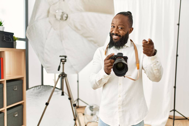 Африканский американский фотограф, работающий в фотостудии, указывает пальцем на камеру со счастливым и смешным лицом. хорошая энергия и вибрации.  - Фото, изображение
