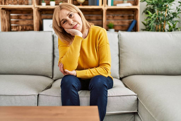 Donna caucasica di mezza età che indossa abiti casual seduta sul divano a casa pensando di sembrare stanca e annoiata con problemi di depressione con le braccia incrociate.  - Foto, immagini