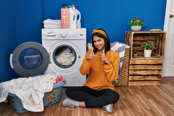 Young hispanic woman doing laundry pointing fingers to camera with happy and funny face. good energy and vibes.  - Foto, Bild