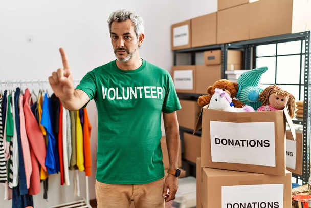 Μεσήλικας Ισπανός που φοράει εθελοντικό μπλουζάκι σε δωρεές στέκεται δείχνοντας με το δάχτυλο ψηλά και θυμωμένη έκφραση, χωρίς να δείχνει καμία χειρονομία  - Φωτογραφία, εικόνα