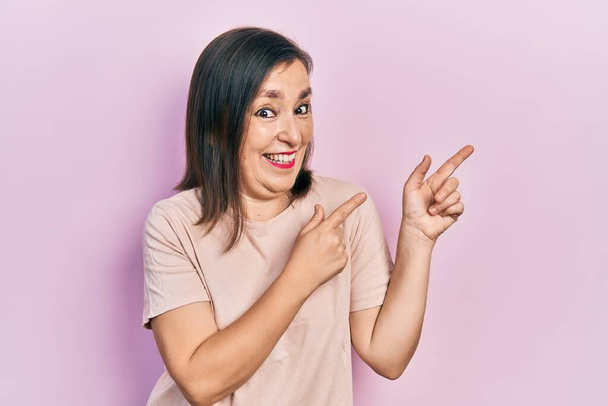Middle age hispanic woman wearing casual clothes smiling and looking at the camera pointing with two hands and fingers to the side.  - Foto, Bild