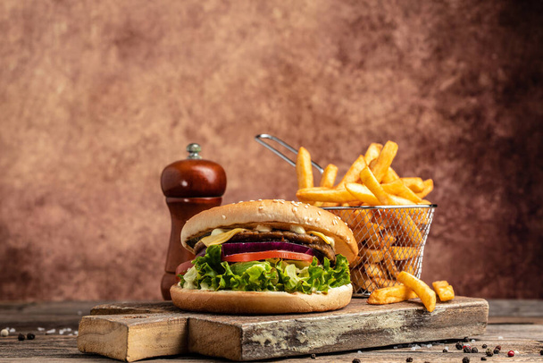 Homemade burger with grilled meat, vegetables, sauce French fries on rustic wooden background. fast food and junk food concept. place for text. - Фото, зображення