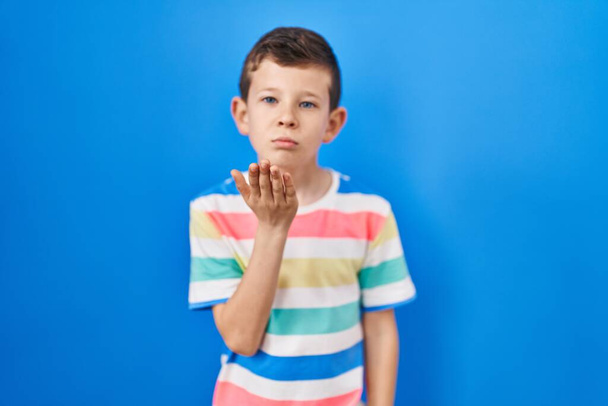 Young caucasian kid standing over blue background looking at the camera blowing a kiss with hand on air being lovely and sexy. love expression.  - Photo, Image