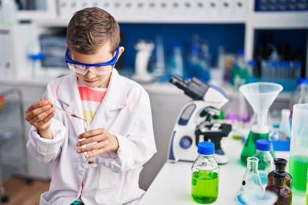 Blond kind draagt wetenschapper uniform met pipet in laboratorium - Foto, afbeelding