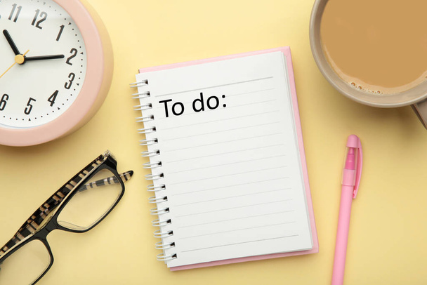 To do list written in a notebook. Notebook with an to do list on pink with cup of coffee and clock. Top view - Фото, изображение