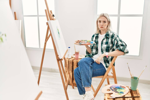 Giovane artista donna pittura su tela in studio d'arte depresso e preoccupazione per l'angoscia, piangendo arrabbiato e spaventato. espressione triste.  - Foto, immagini