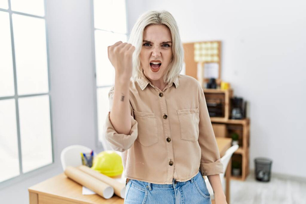 Young beautiful caucasian woman at construction office angry and mad raising fist frustrated and furious while shouting with anger. rage and aggressive concept.  - Фото, зображення