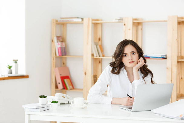 Zmęczony piękna bizneswoman, trzymając rękę na głowie podczas pracy na komputerze i niektórych dokumentów biznesowych w biurze jasne - Zdjęcie, obraz