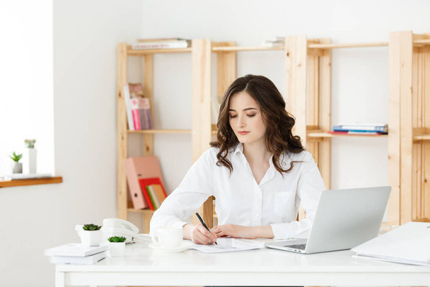 Giovane donna attraente presso una scrivania moderna ufficio, lavorando con il computer portatile e pensando a qualcosa
. - Foto, immagini