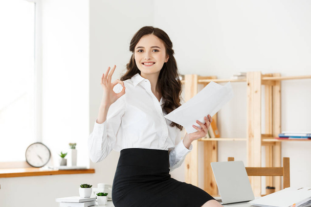 Ділова жінка в офіційному носінні, що тримає документи і показує знак ОК в сучасному офісі, копіювати простір
. - Фото, зображення