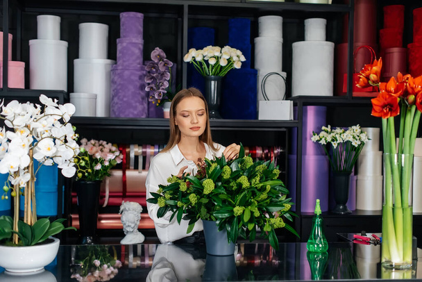 A young female florist takes care of flowers in a cozy flower shop and collects bouquets. Floristry and making of bukets in a flower shop. Small business. - Fotografie, Obrázek