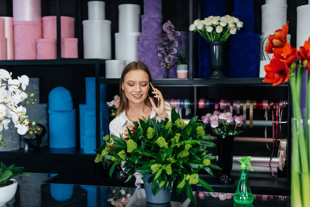 A young woman florist accepts an order by phone for the production of a beautiful festive bouquet. Floristry and making of bukets in a flower shop. Small business. - Photo, Image