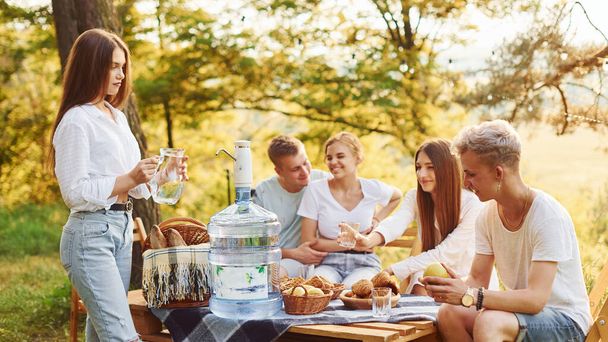 Big plastic water bottle on table. Group of young people have vacation outdoors in the forest. Conception of weekend and friendship. - Foto, Imagem