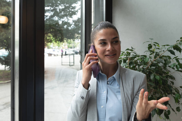 Young business woman in casual suit standing near window in the restaurant holding her smartphone waiting to waiter pack her lunch to go in the box. Freelancer expat waiting take away coffee or food. - Foto, Bild