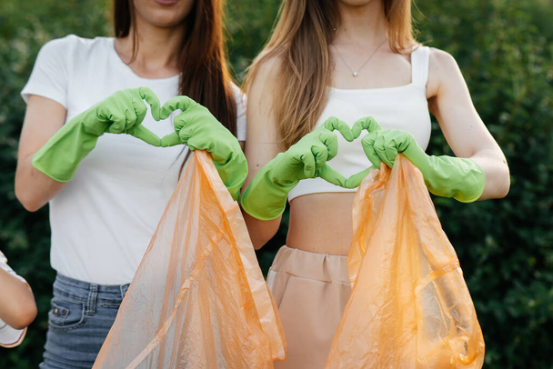 Young women shows hearts after garbage collection in the park during sunset. Environmental care, waste recycling. Sorting garbage. - Fotoğraf, Görsel