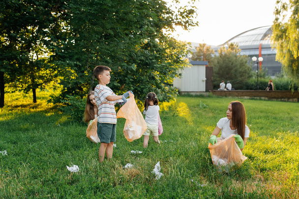 A group of adults and children together at sunset is engaged in garbage collection in the park. Environmental care, waste recycling. Sorting garbage. - Фото, зображення