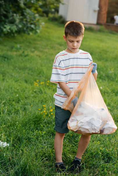 A seven-year-old boy at sunset is engaged in garbage collection in the park. Environmental care, recycling. - Photo, Image