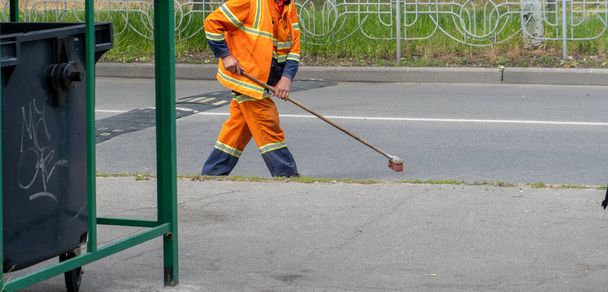 Man cleaner sweeping street with broom, municipal worker in uniform with broomstick brush for garbage in hands, cleaning service. Male janitor with broom , cleaning city from garbage. - Zdjęcie, obraz